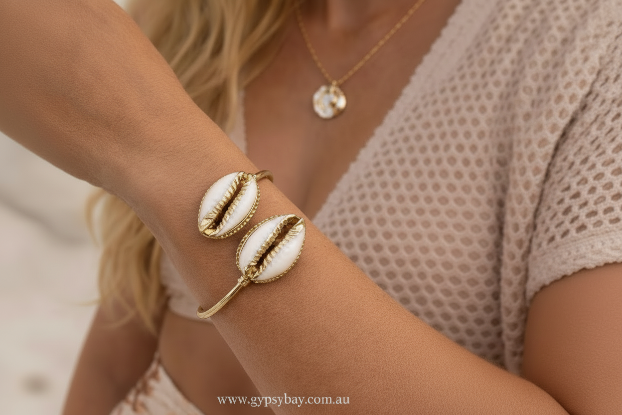 Gold cowrie shell bracelet with shell design on a wrist, blurred background