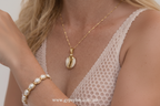 Gold necklace with a cowrie shell pendant worn by a person, close-up view.