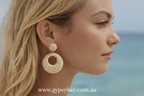 Close-up of a woman wearing gold hoop earrings with a blurred beach background