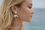 Close-up of a woman wearing palm tree-shaped earrings with a blurred beach background