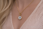 Gold necklace with a round pendant featuring a blue design on a person wearing a lace garment.