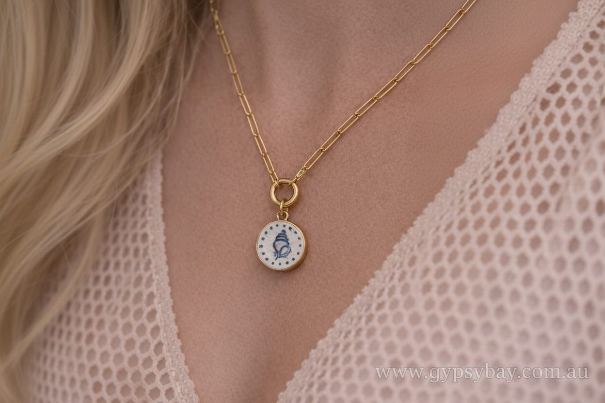 Gold necklace with a round pendant featuring a blue design on a person wearing a lace garment.
