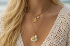 Gold necklace with starfish and shell pendants worn by a person with blonde hair.