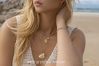 Woman wearing gold necklaces with starfish and shell pendants outdoors.