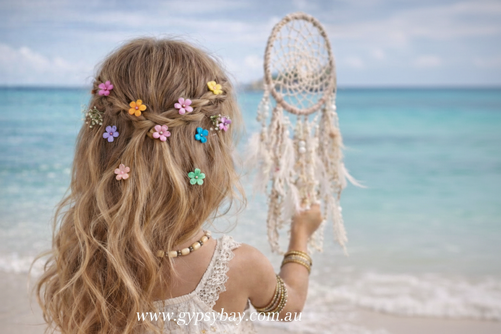 child with braided hair adorned with colorful flowers, holding a dreamcatcher on a beach.